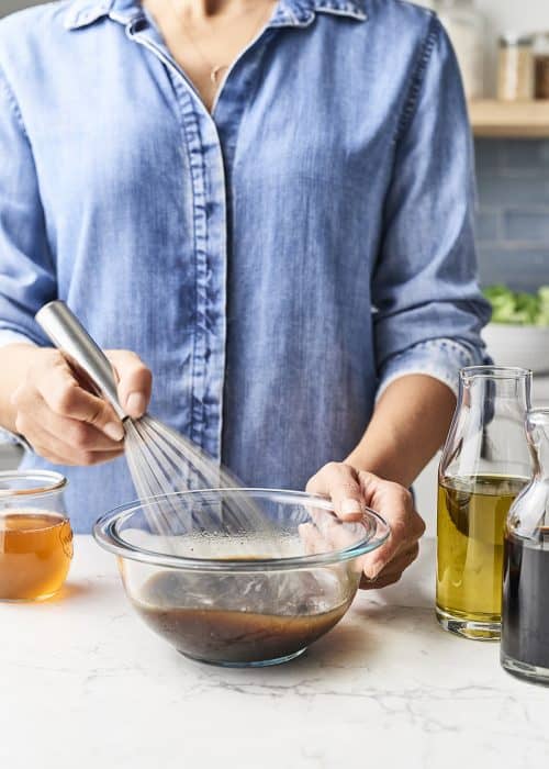 Woman whisking fresh homemade versatile pantry salad dressings on a white marble counter in a beautiful kitchen