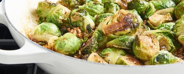 Golden brown candied brussels sprouts in a white skillet on a stovetop