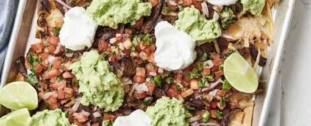 Loaded sheet pan of The Fresh 20 shredded steak nachos with guacamole clean eating meal plan service recipe with lime wedges