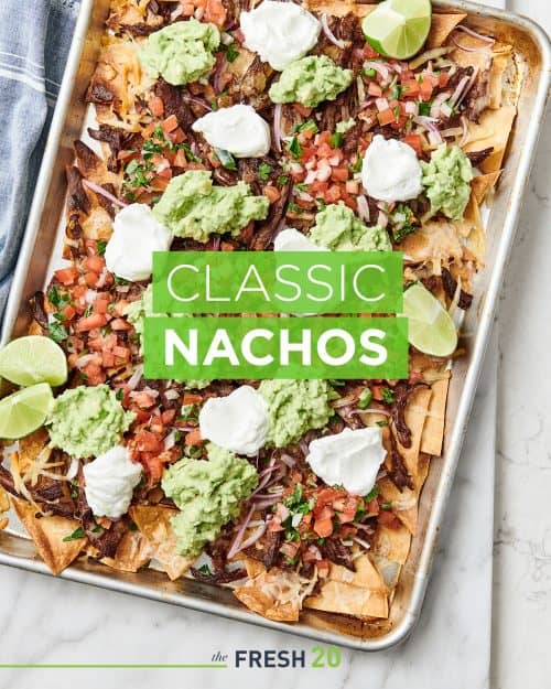 Sheetpan loaded with steak nachos with pico de gallo, sour cream and guacamole on a white marble surface