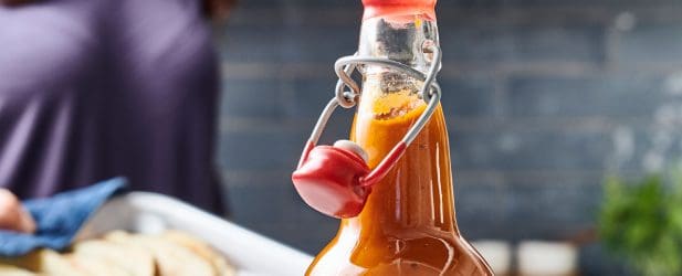 Woman in kitchen cooking homemade ketchup holding a pan in a marble kitchen