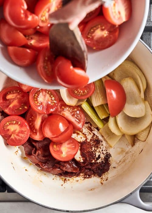 Pot full of vibrant tomatoes and vegetables cooking on the stove from above