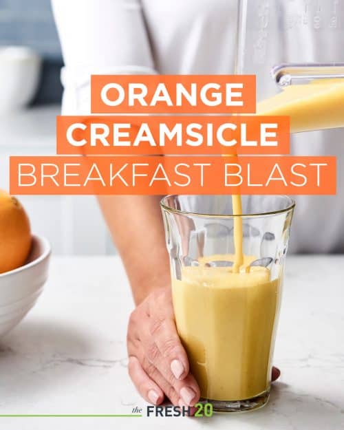 Woman pouring orange creamsicle smoothie into a glass in a white marble kitchen