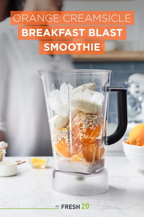 Woman making a smoothie with fresh oranges and bananas in a blender in a beautiful white marble kitchen