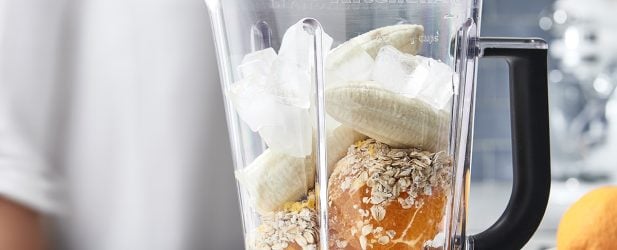 Woman making a smoothie with fresh oranges and bananas in a blender in a beautiful white marble kitchen