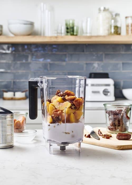 Blender on a white marble surface full of fresh and frozen fruit making tropical peach sorbet in a beautiful kitchen