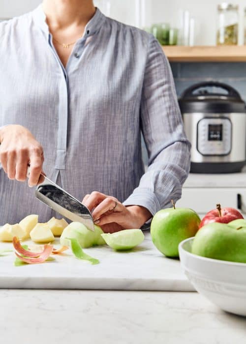 Woman slicing green apples on a white marble surface with an Instant Pot on the back counter in a beautiful modern kitchen