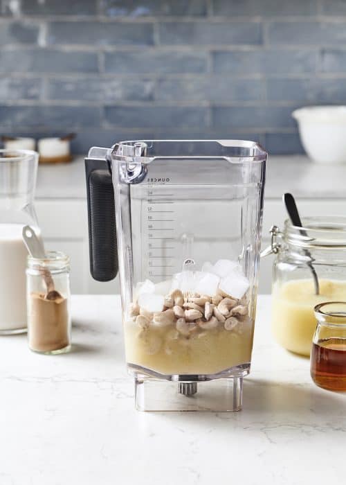 Blender full of easy healthy apple pie smoothie ingredients on a white marble surface in a beautiful kitchen