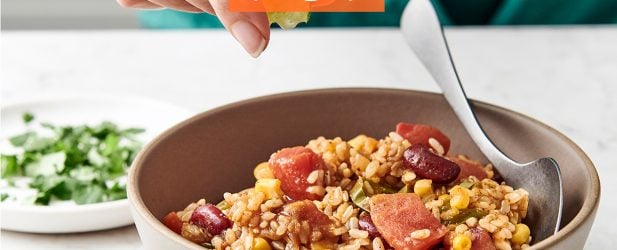 Woman squeezing a lime wedge into a hearty bowl of The Fresh 20 Vegetarian Spanish Instant Pot Crock-Pot recipe