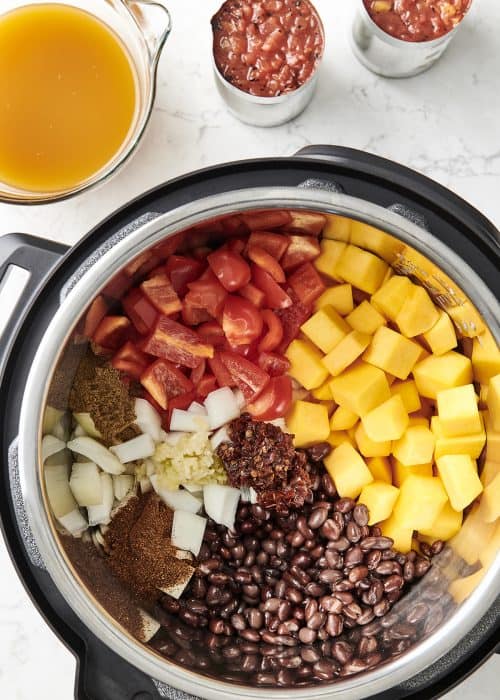 Vegetarian chipotle chilli fresh organized ingredients inside an Instant Pot Crock-Pot on a white marble surface from above