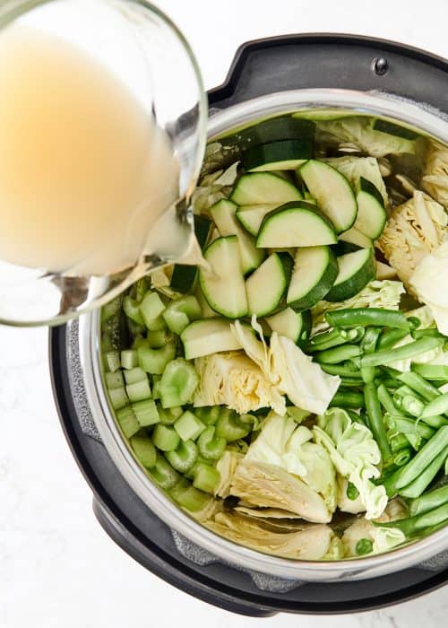 Instant Pot full of green vibrant ingredients with vegetable stock being poured