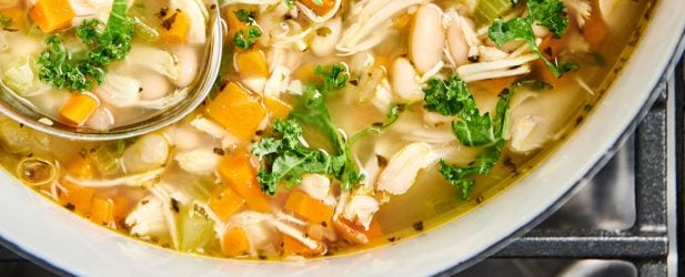 Le Creuset pot of simple hearty weeknight chicken soup with carrots and kale on the stove with a ladle from above