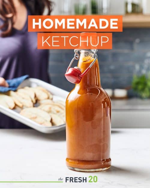 Cool jar of homemade DIY ketchup on a white marble counter in a beautiful kitchen with woman holding a pan of fries