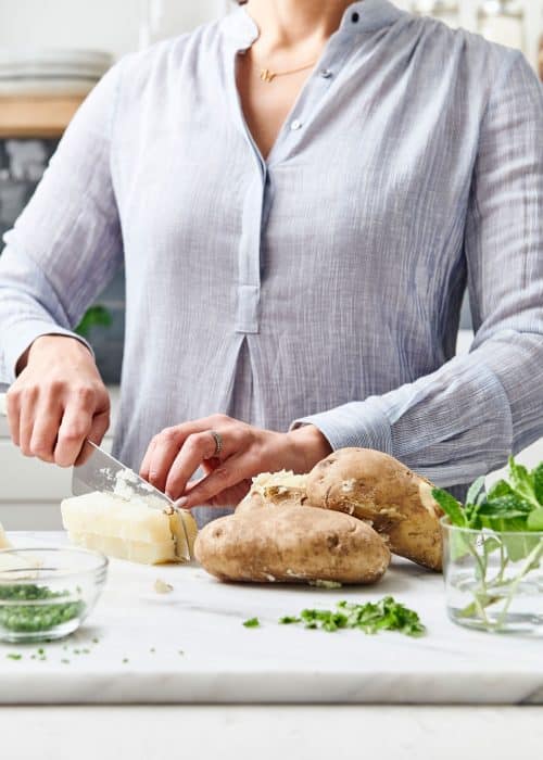 Woman chopping potatoes and garnishes on a pretty marble surface