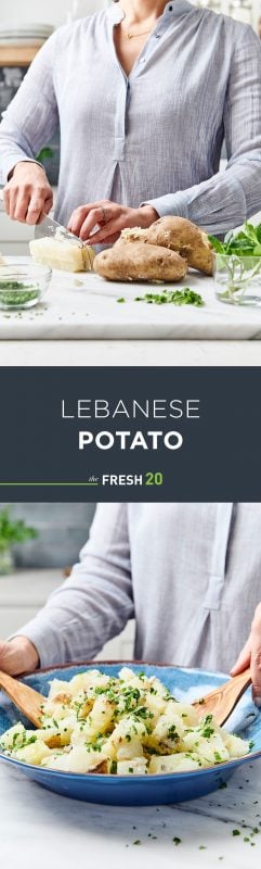 Woman prepping and mixing potatoes garnished with chives in a blue bowl with wooden spoons on a white marble surface