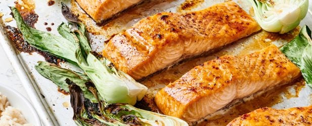 A baking sheet pan loaded with maple soy salmon recipe surrounded with bok choy