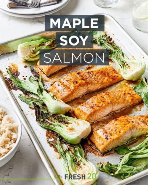 A baking sheet pan loaded with maple soy salmon recipe surrounded with vibrant bok choy and a bowl of rice