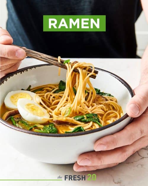 Man using chopsticks in a ceramic bowl of suculent ramen noodles with mushroom, spinach & soft boiled egg