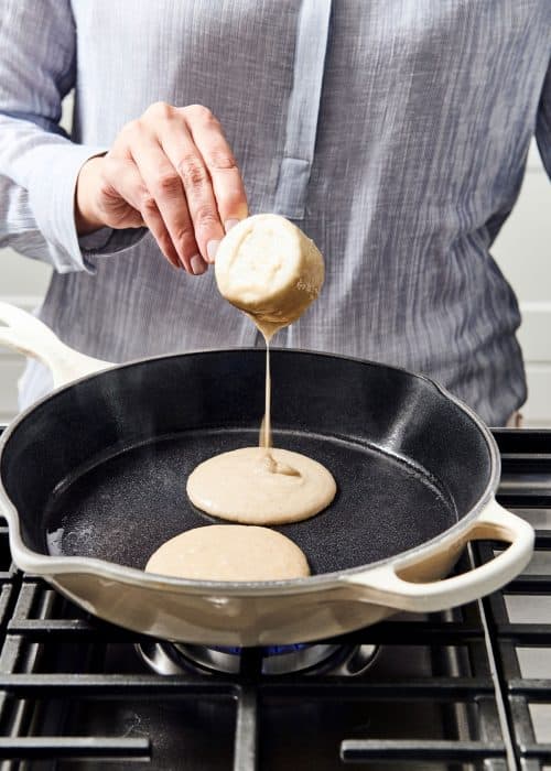 Woman pouring creamy paleo pancake batter into skillet on a gas cooktop