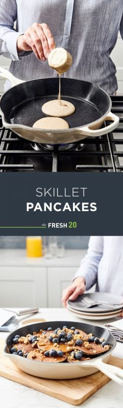 Skillet full of fluffy pancakes with plump blueberries, crushed nuts & syrup in a white marble kitchen