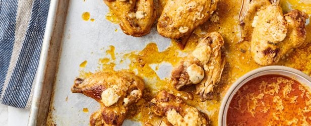 Baking sheet pan full of buffalo wings with a bowl of dipping sauce