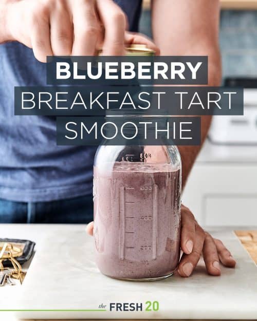 Man opening glass mason jar full of creamy decadent vegan blueberry breakfast tart smoothie in a white marble finished kitchen