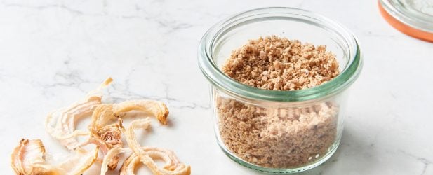 Small Weck glass jar filled with DIY homemade onion powder alongside dried onions on a white marble surface