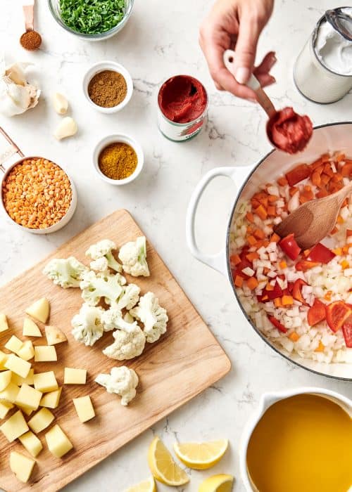 Overhead view of ingredients and spices on a wood cutting board and in a white stockpot for a vegan red lentil curry