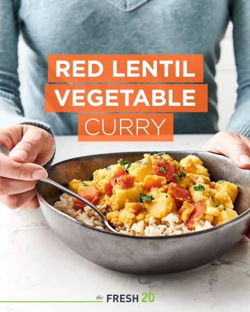 Woman eating a vibrant hearty vegan curry in a black ceramic bowl on a white marble countertop