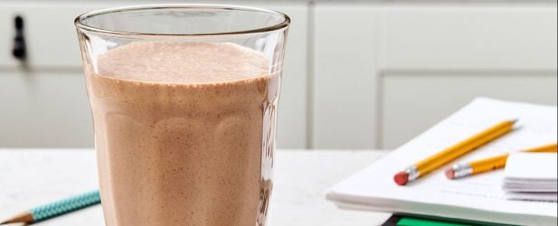 Afterschool chocolate protein shake in a tall clear glass next to school supplies