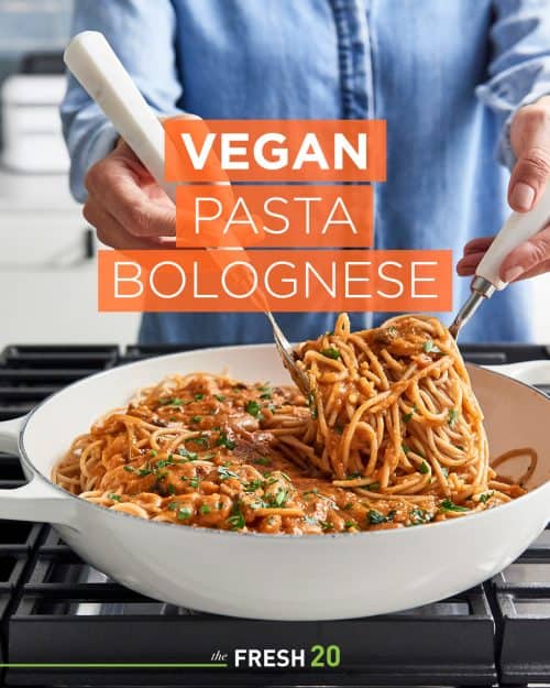 Woman scooping vegan bolognese with two white serving utensils from a skillet on a cooktop