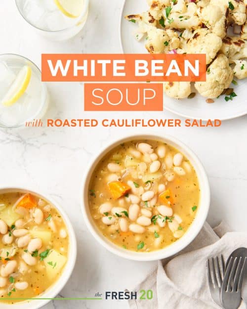 Two cream colored bowls full of hearty white bean soup alongside roasted cauliflower and two water glasses with lemon slices