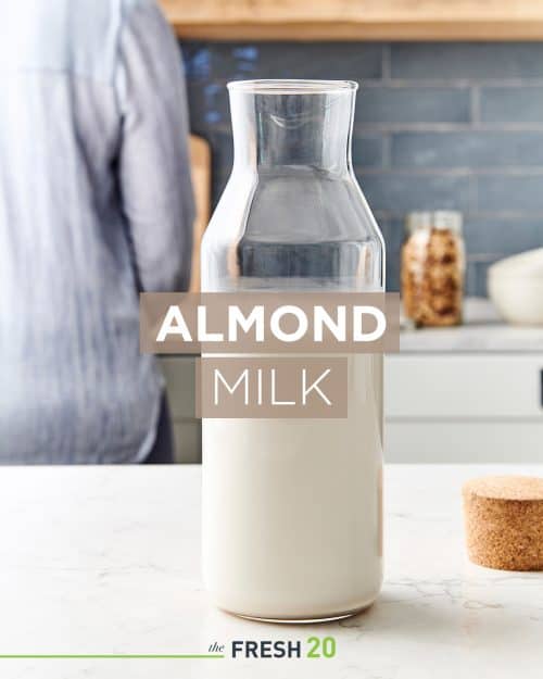 Beautiful tall glass milk jug full of creamy easy homemade almond milk in a white marble kitchen