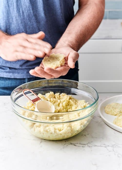 Man shaping cauliflower hashbrowns and placing them onto a ceramic plate in a white marble kitchen