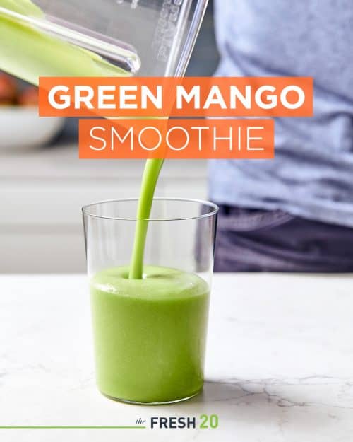 Person pouring tropical green mango smoothie into a clear modern glass in a beautiful white marble kitchen