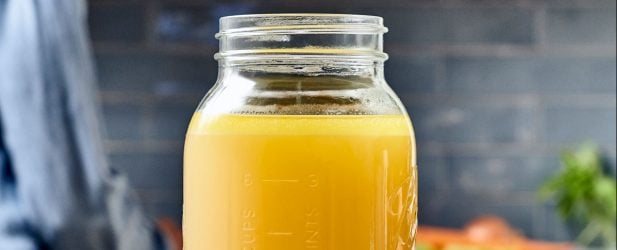 Large mason jar filled with fresh homemade chicken broth in a beautiful kitchen