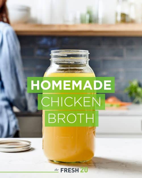 Large mason jar filled with fresh homemade chicken broth in a beautiful white marble kitchen