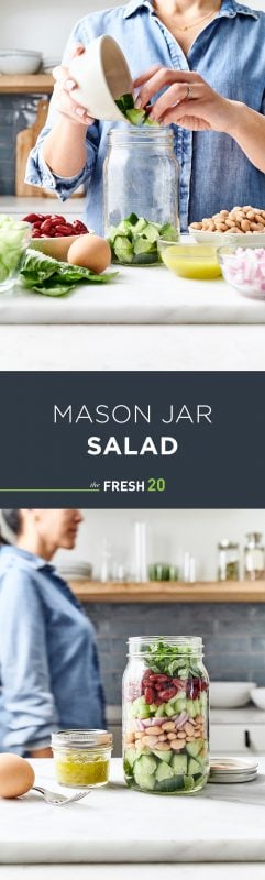 Woman filling & walking by a mason jar full of salad next to a mini jar of dressing & a hard boiled egg in a white marble kitchen