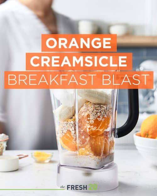 Woman making a smoothie with fresh oranges and bananas in a blender in a beautiful white marble kitchen