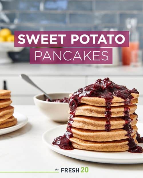 Tall stack of fluffy sweet potato pancakes on a cream plate coated in a thick sweet blueberry compote in a white marble kitchen