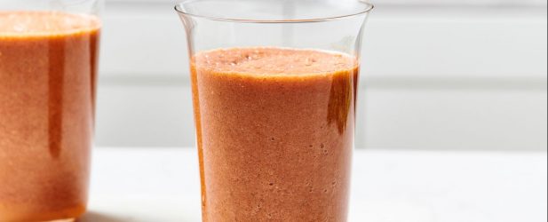 Tall modern glasses full of fresh tomato juice on a white marble surface