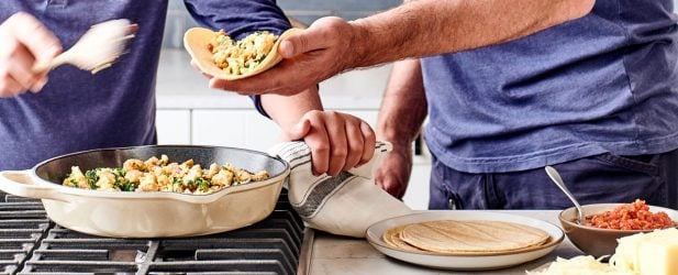 Father and son using tortillas to wrap burritos filled with egg mixture in a beautiful marble kitchen