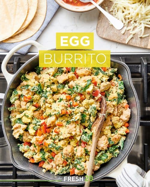 Skillet filled with scrambled egg mixture with salsa, cheese and tortillas on a white marble countertop