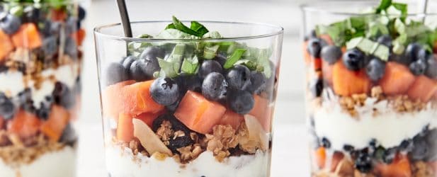 3 parfait glasses filled with layers of homemade granola, fruit & greek yogur in a beautiful white marble kitchen