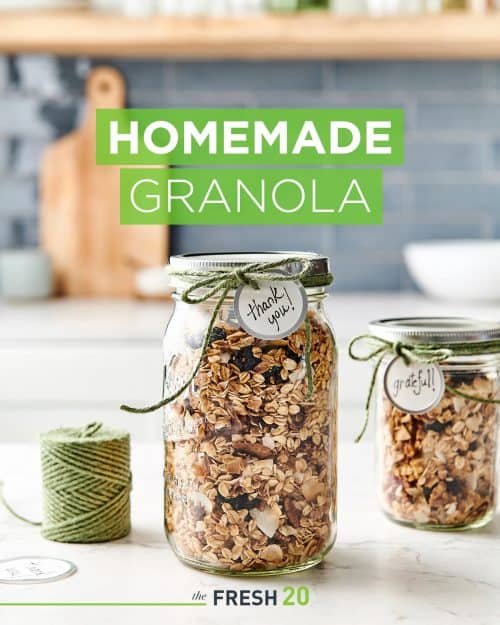 2 mason jars full of decadent homemade DIY granola wrapped with a green twine & a thank you tag on a white marble surface