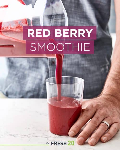 Man pouring a deep rich red beet smoothie in a clear thin glass in a beautiful white marble kitchen