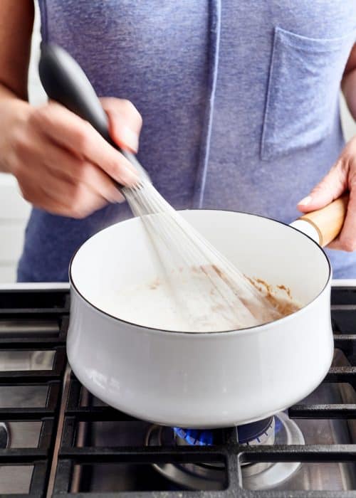 Woman whisking paleo almond pancake batter in a white pot on a gas cooktop