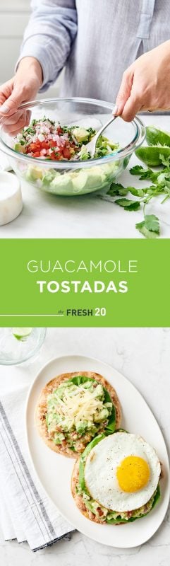 Woman mashing avocados, tomatoes & onions with a fork in a glass bowl for guacamole tostadas with lime and cilantro on a white marble surface