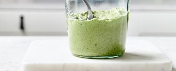 Glass Weck jar full of vibrant fresh homemade pesto with a spoon on a white marble surface in a beautiful modern kitchen