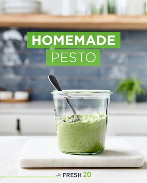 Glass Weck jar full of vibrant fresh homemade pesto with a spoon on a white marble surface in a beautiful modern kitchen